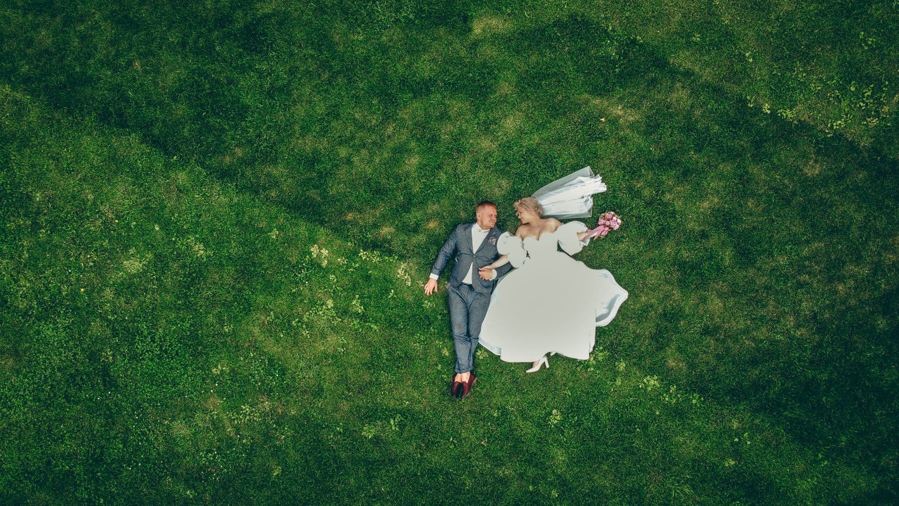 Mire și mireasă fotografiați de sus, din dronă, pe iarbă